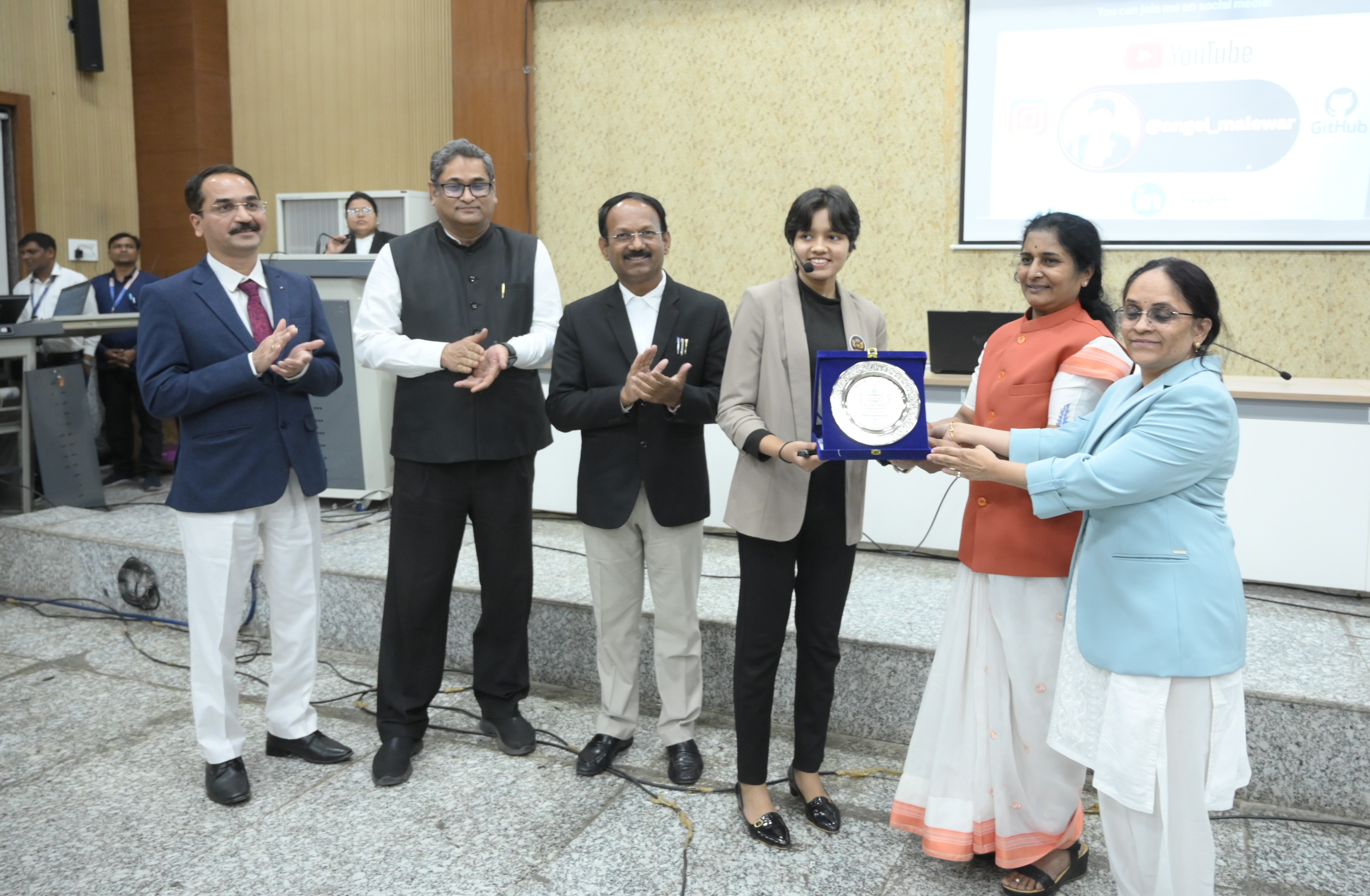 Angel Malewar receiving a recognition plaque at an institutional event